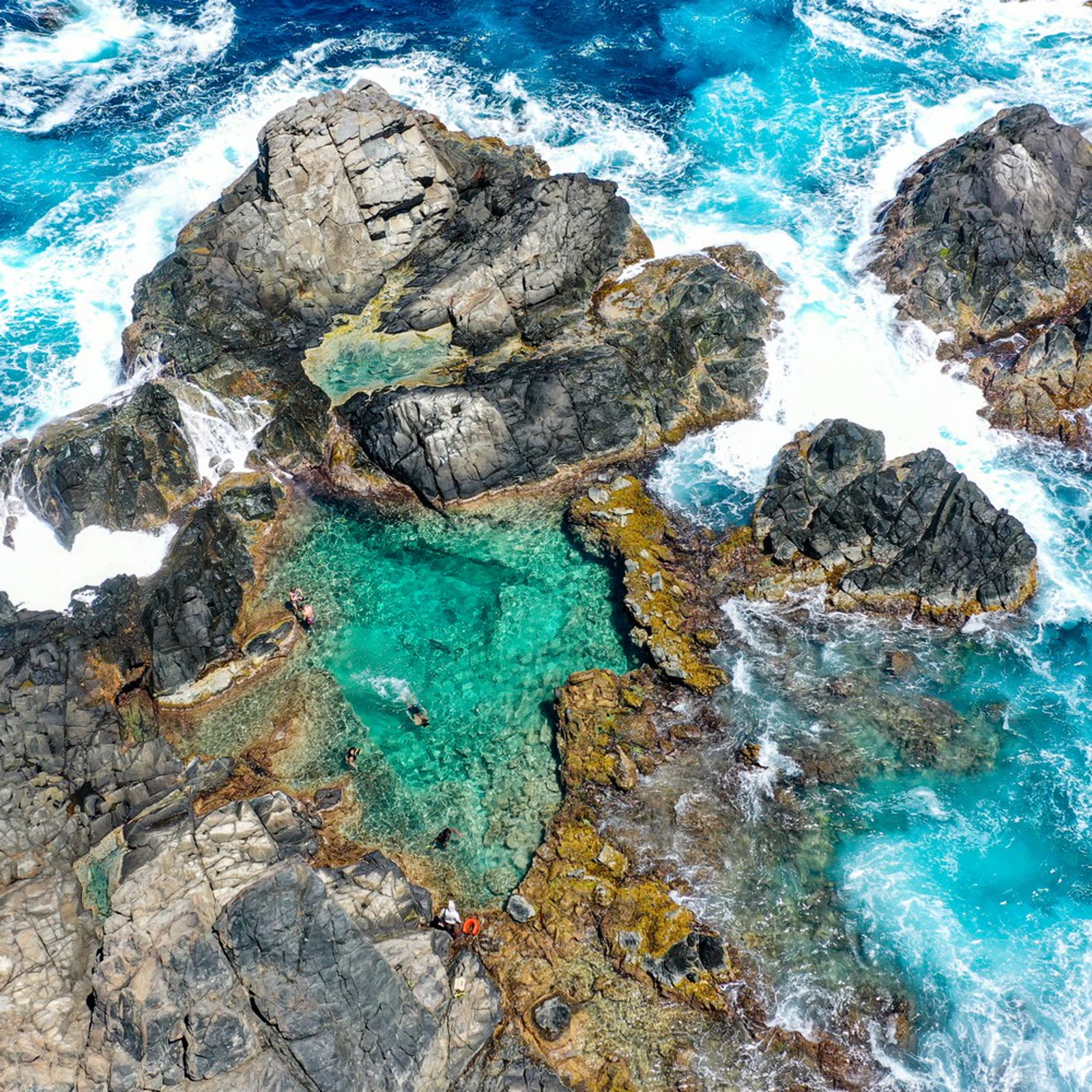 Aerial view of the Natural Pool, a turquoise basin enclosed by dark volcanic rock