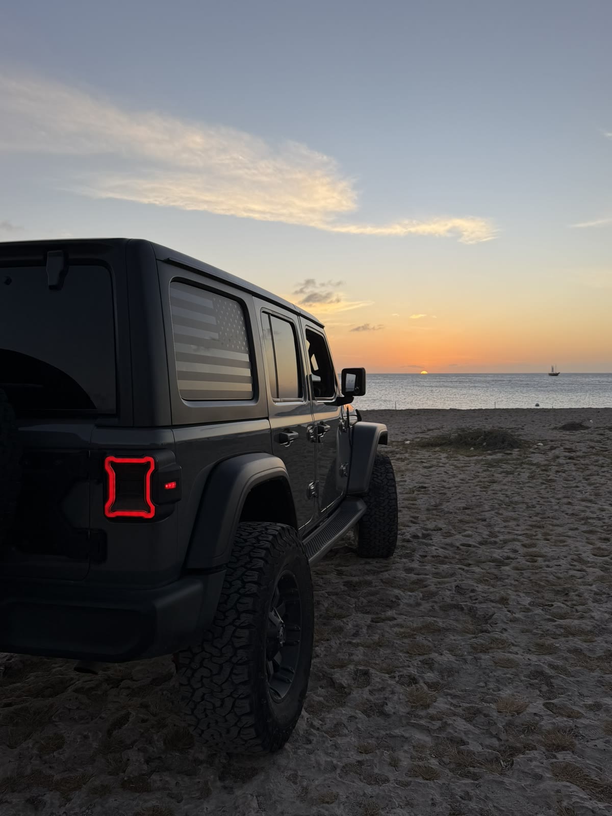 A Jeep on a dark sand beach at sunset
