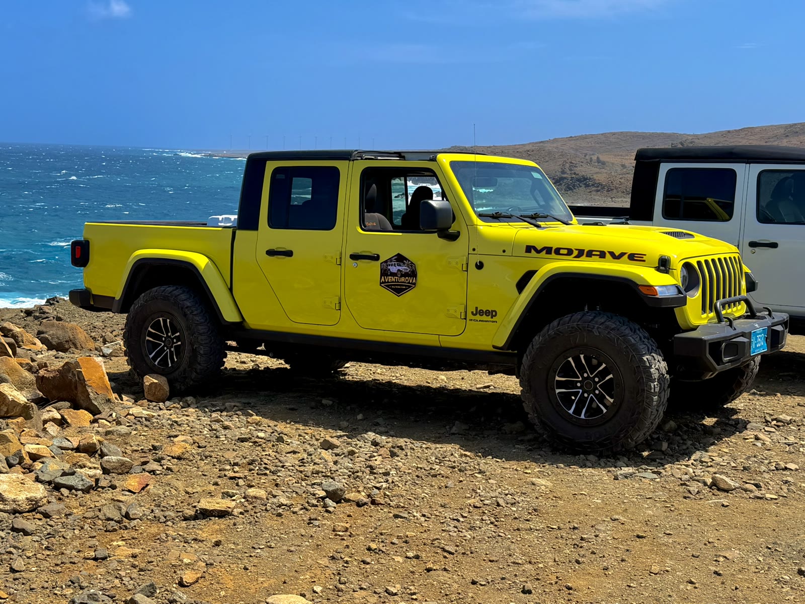 Yellow Jeep Gladiator parked on rocky ground above the sea