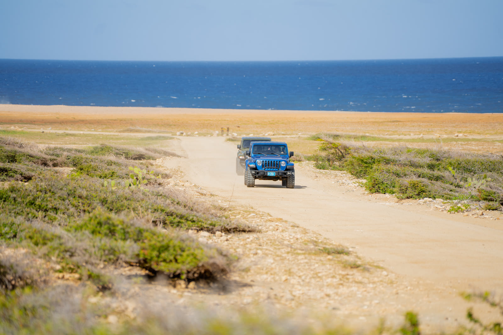Blue Jeep Gladiator driving along a sandy coastal track