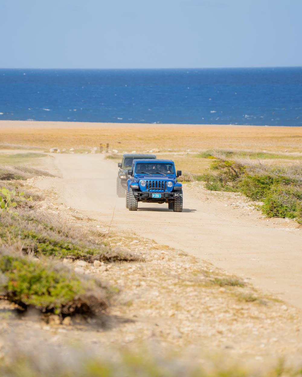 Blue Jeep driving along a sandy track with the sea on the horizon