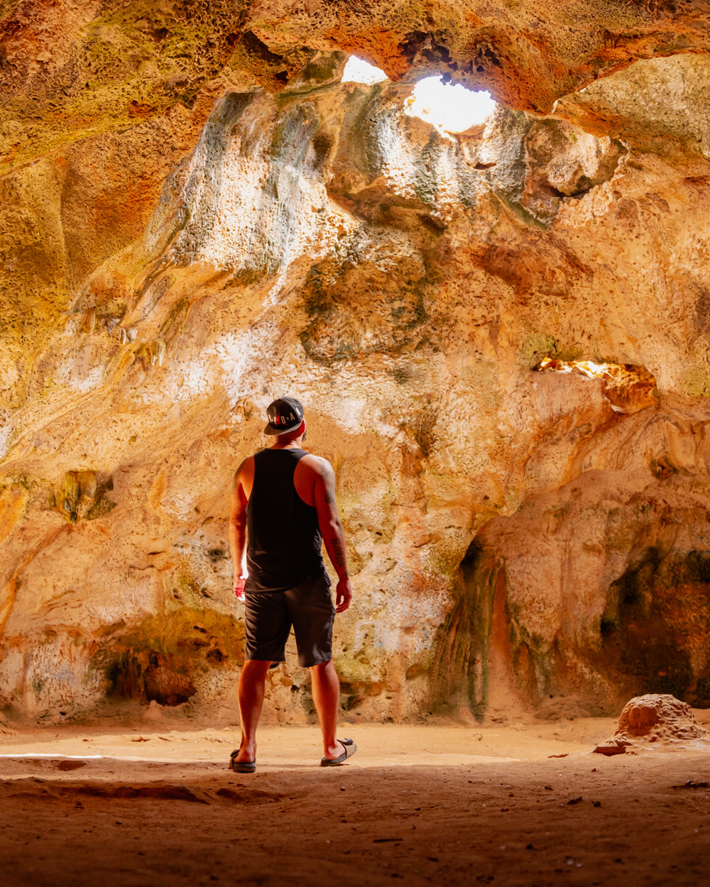 A person standing inside Quadirikiri cave while light comes in through openings in the ceiling