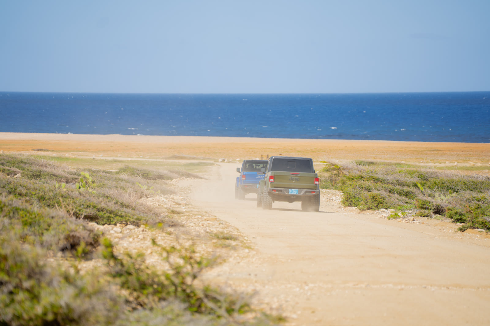 Two Jeeps driving away along a sandy coastal track