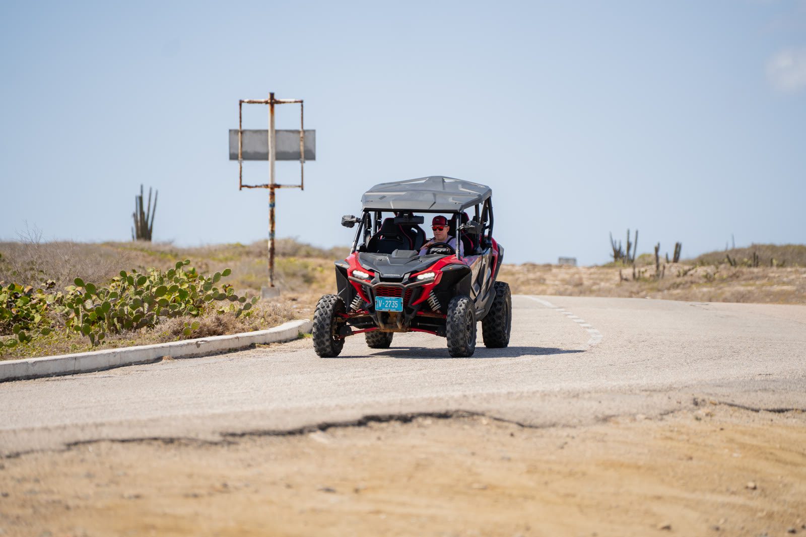 A red UTV driving on a sandy road with low scrub