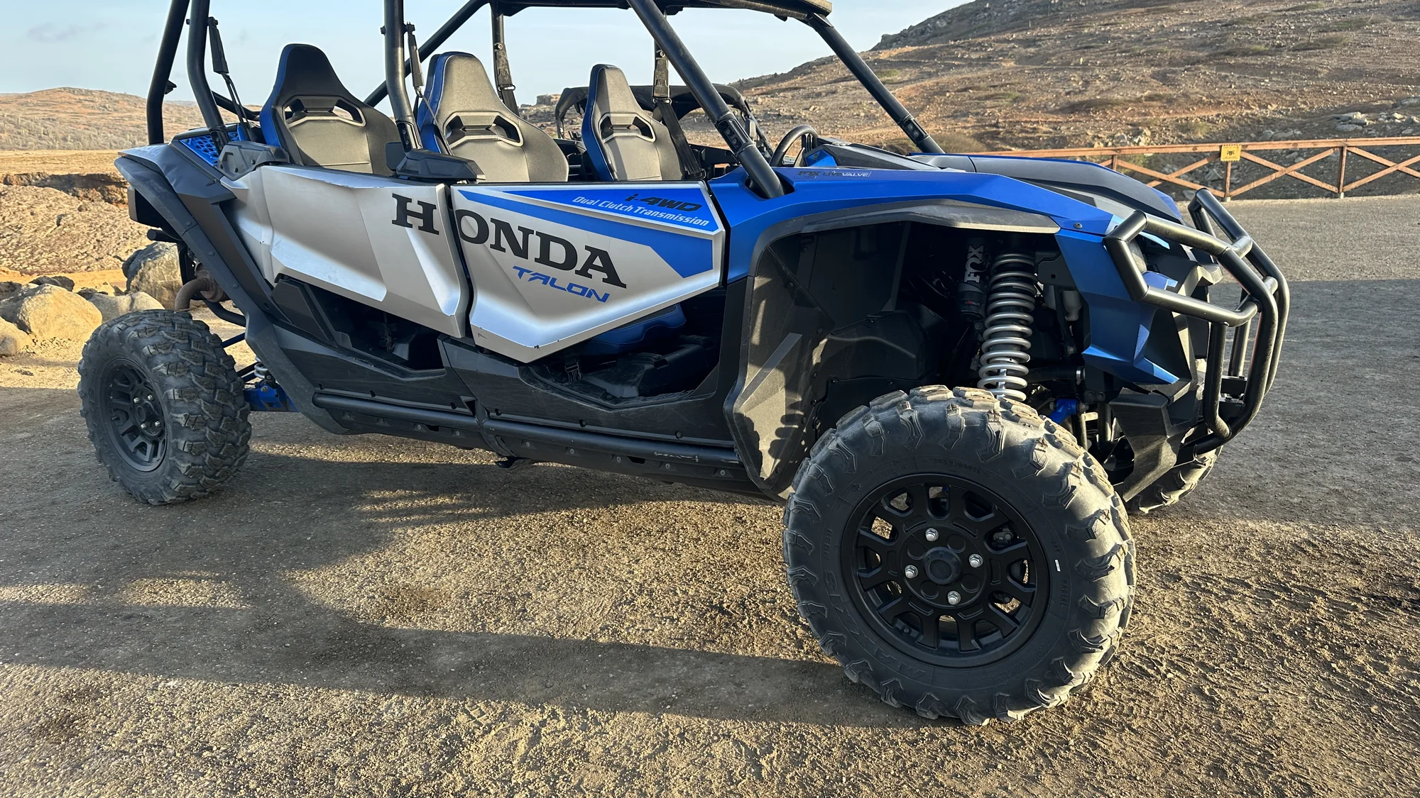 Blue Honda Talon UTV with a roll cage and seats side by side on a dirt lot
