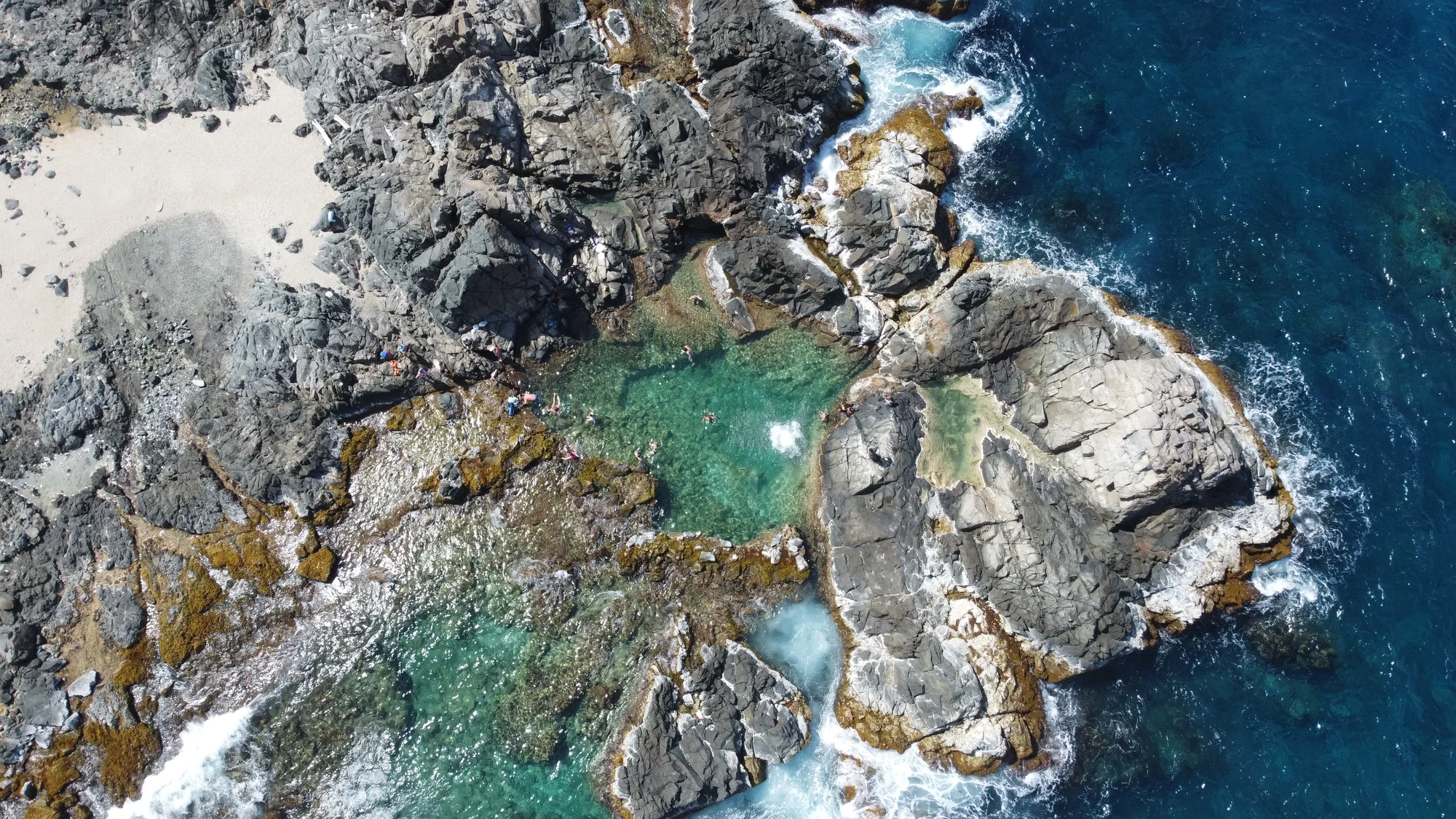 Visitors posing for a photo on rocky ground beside a rock arch over the sea
