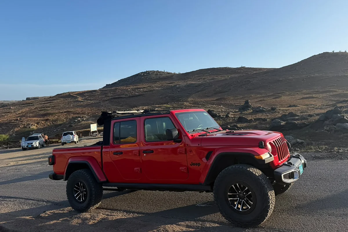 Red Aventurova Jeep Gladiator parked on a road below brown hills on Aruba's north coast